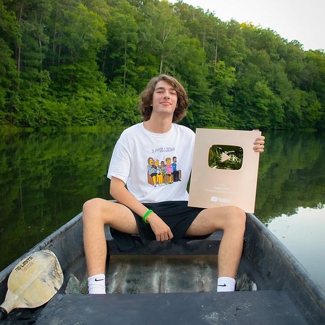 Baylen Levine in a white t-shirt and black shorts holding a YouTube silver play button.